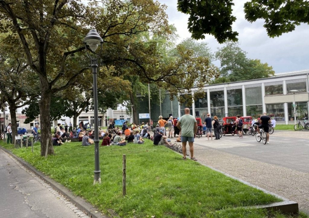 Foto der Kundgebung am Frankenbadplatz in Bonn von weitem. Es sind die Teilnehmer*innen der Kundgebung der Disability und Mad Pride Bonn zu sehen.
