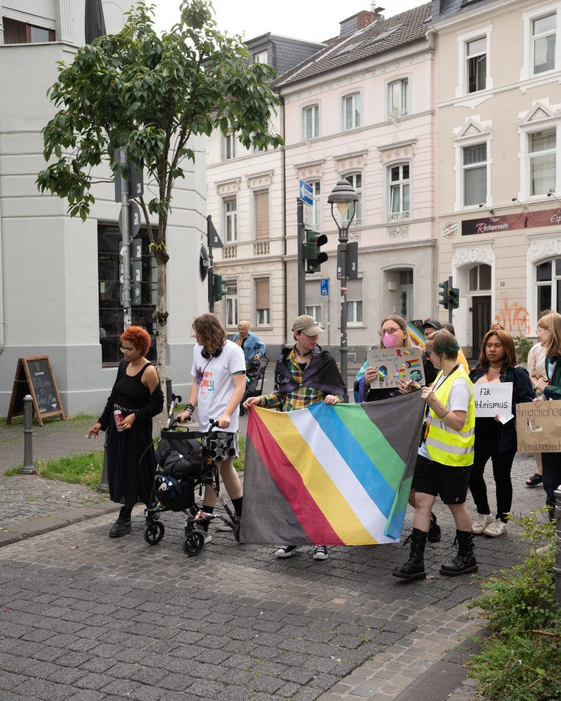 Foto der Laufdemo von vorne, mit Disability Pride Flagge.